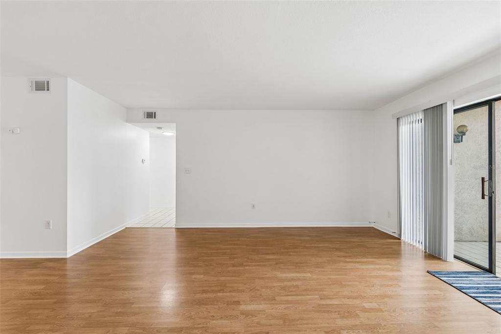An empty living room features light wood-look flooring, white walls, and a sliding glass door — 2971 ESTANCIA BOULEVARD UNIT 313, CLEARWATER, FL