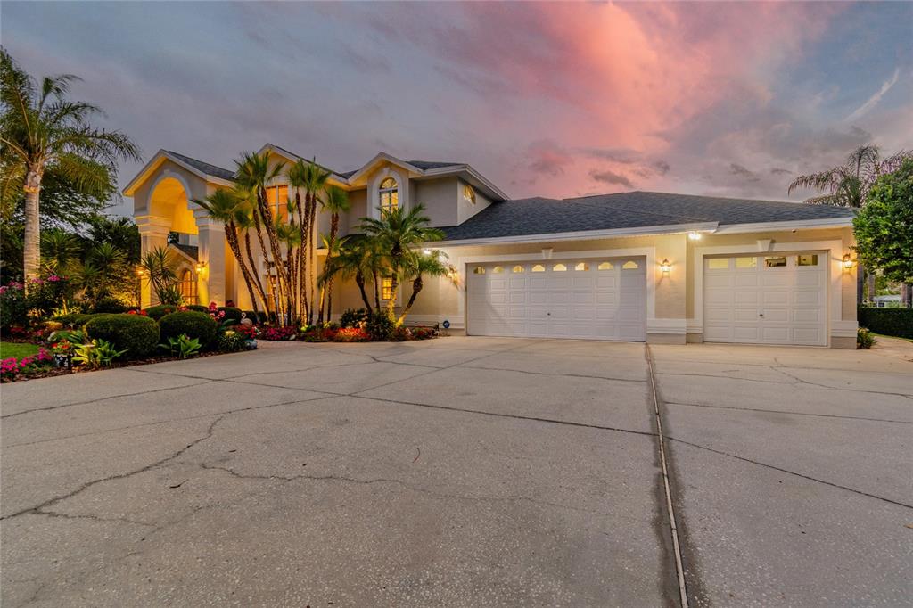 A two-story house with a three-car garage and palm trees under a sunset sky — 5851 CACHETTE DE RIVIERA COURT, NEW PORT RICHEY, FL