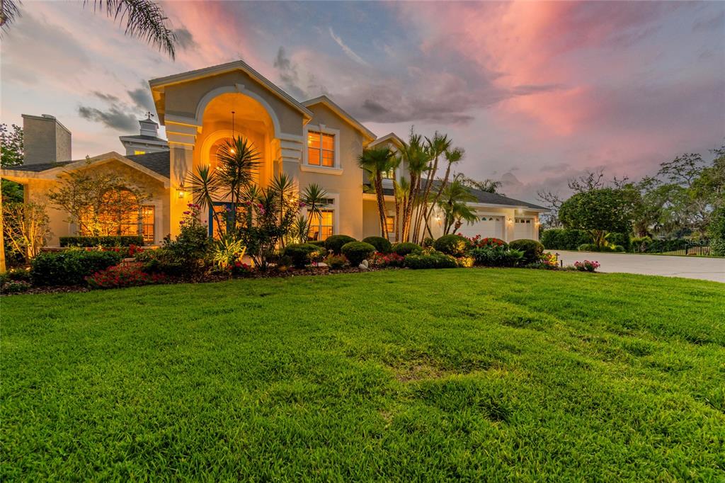 A two-story house with a large arched entryway and palm trees at sunset — 5851 CACHETTE DE RIVIERA COURT, NEW PORT RICHEY, FL