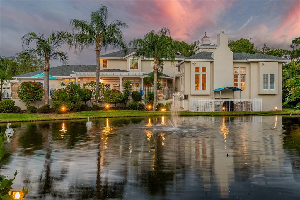 A large two-story house with a fountain in a pond and palm trees at sunset — 5851 CACHETTE DE RIVIERA COURT, NEW PORT RICHEY, FL