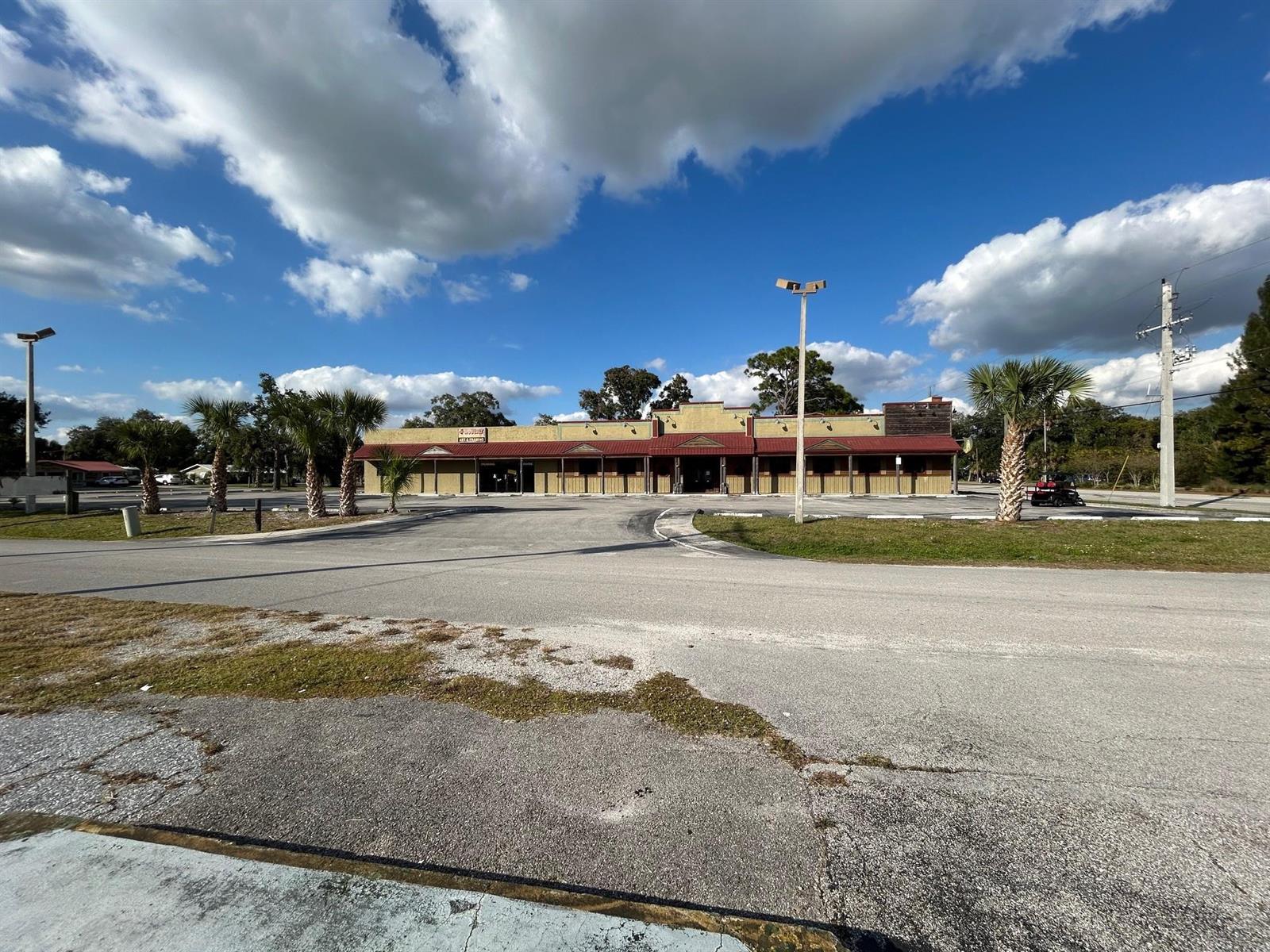 A single-story commercial building with a red metal roof sits behind a large parking lot — 102 SW 14th Street, Okeechobee FL 34974, OKEECHOBEE, FL