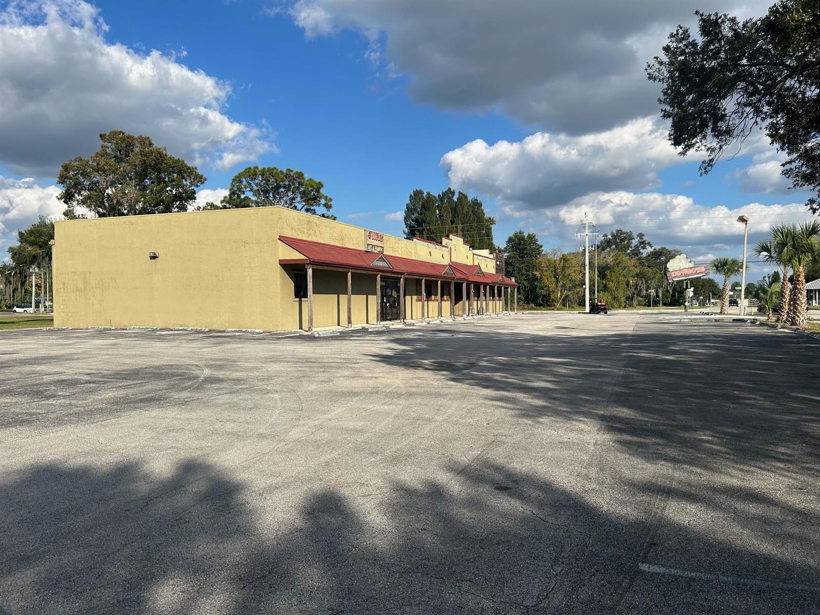 A tan commercial building with a red metal awning sits beside a large asphalt parking lot — 102 SW 14th Street, Okeechobee FL 34974, OKEECHOBEE, FL