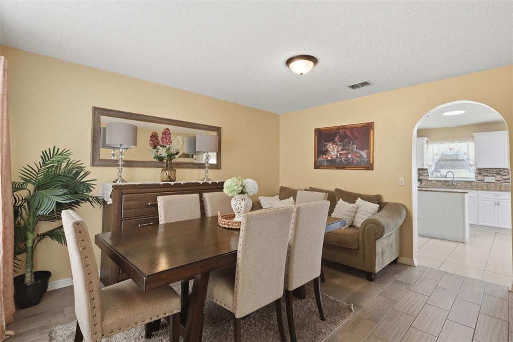 A dining room features a wooden table, upholstered chairs, a sideboard with a mirror, and a sofa — 1142 NORMANDY DRIVE, KISSIMMEE, FL
