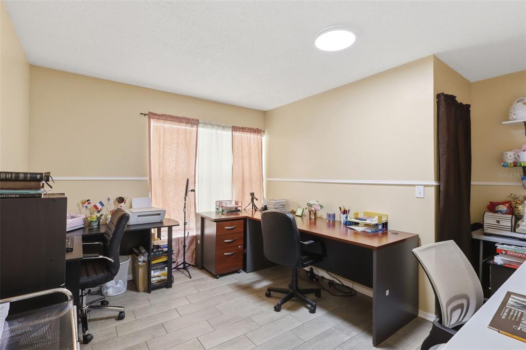 A home office features tile flooring, beige walls, and multiple desks with office chairs — 1142 NORMANDY DRIVE, KISSIMMEE, FL