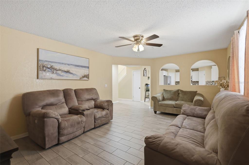A living room features light-colored tile flooring, beige walls, two brown sofas, and a ceiling fan — 1142 NORMANDY DRIVE, KISSIMMEE, FL