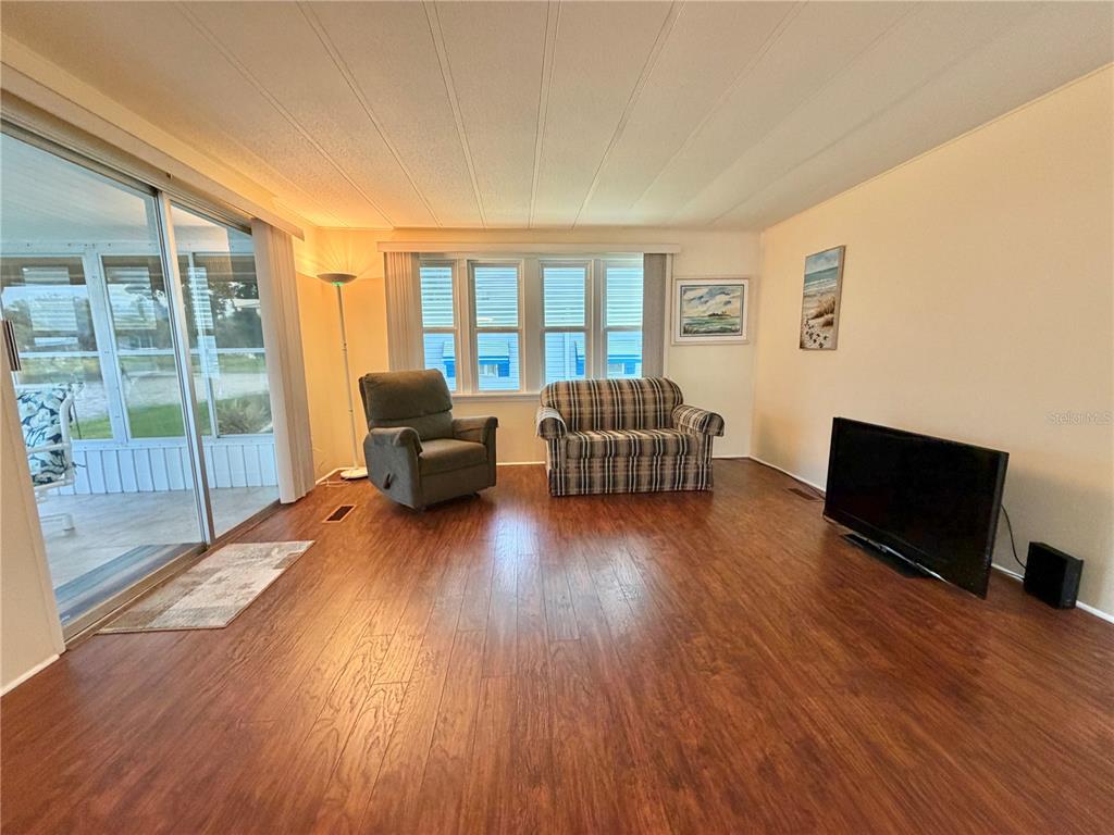 A living room with wood-look flooring, a recliner, a plaid sofa, and an adjacent kitchen — 119 AUDUBON DRIVE, LEESBURG, FL