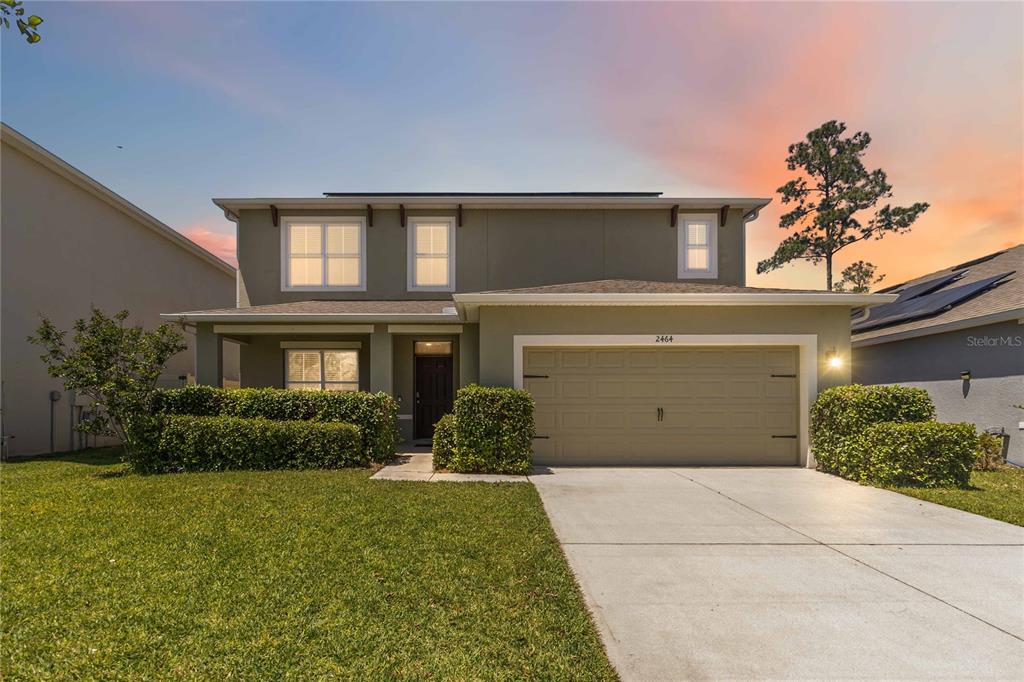 A two-story house with a beige exterior, a two-car garage, and a manicured front lawn — 2464 WHITE POPPY DRIVE, KISSIMMEE, FL
