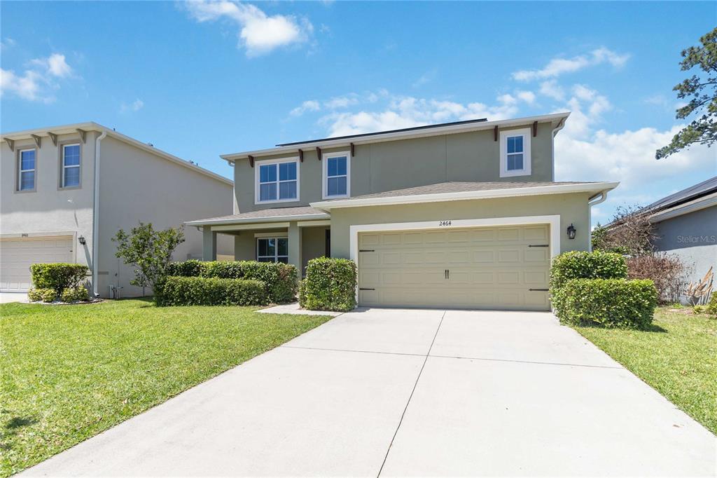 A two-story suburban house with a beige garage, green siding, and a concrete driveway — 2464 WHITE POPPY DRIVE, KISSIMMEE, FL