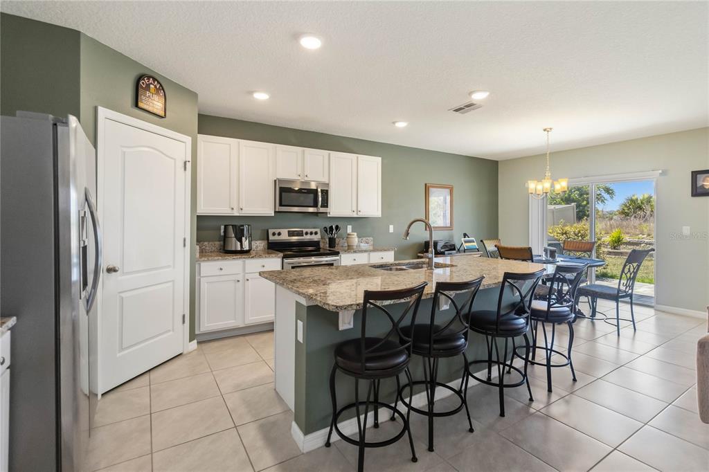 A kitchen with white cabinets, granite countertops, a center island with bar stools, and tile flooring — 2464 WHITE POPPY DRIVE, KISSIMMEE, FL