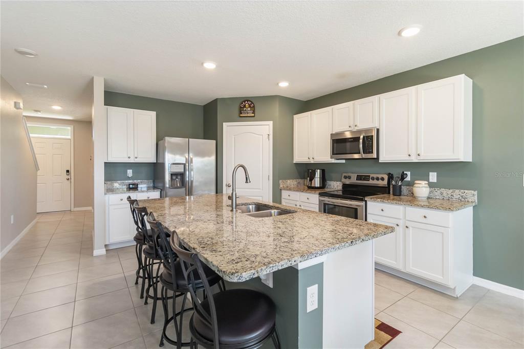 A kitchen features white cabinets, granite countertops, a central island with seating, and stainless appliances — 2464 WHITE POPPY DRIVE, KISSIMMEE, FL