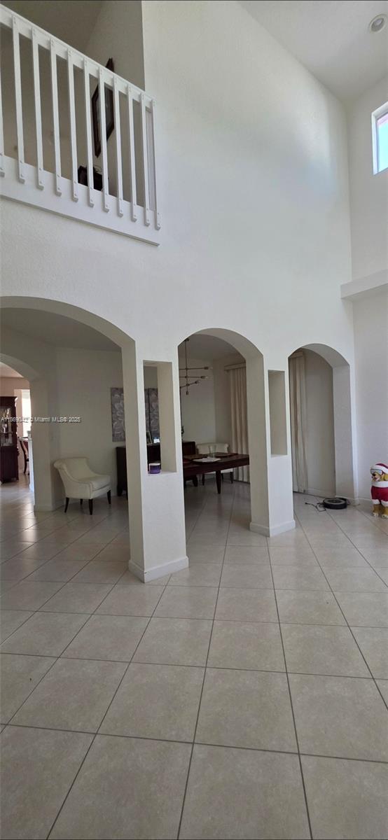 A high-ceilinged living area features arched openings, tiled floors, and a white balcony railing — 16448 SW 67th Ter, Miami FL 33193, MIAMI, FL