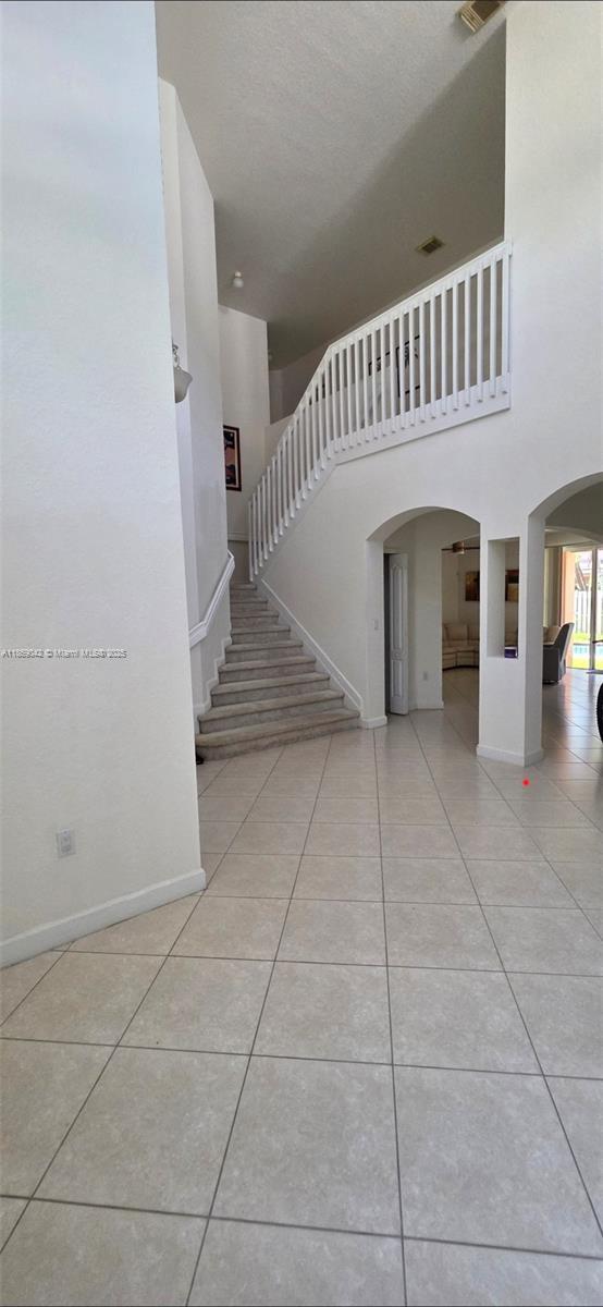 A bright foyer features light tile flooring, a carpeted staircase, and a white wooden railing — 16448 SW 67th Ter, Miami FL 33193, MIAMI, FL
