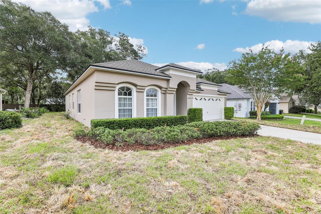 A single-story beige stucco house features arched windows, a two-car garage, and landscaped shrubbery — 30254 PGA DRIVE, SORRENTO, FL
