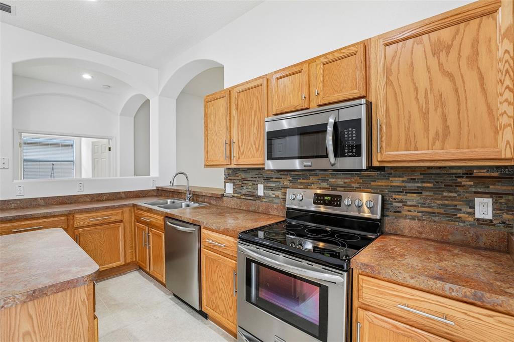 A kitchen features oak cabinets, stainless steel appliances, and a multi-colored stone tile backsplash — 30254 PGA DRIVE, SORRENTO, FL