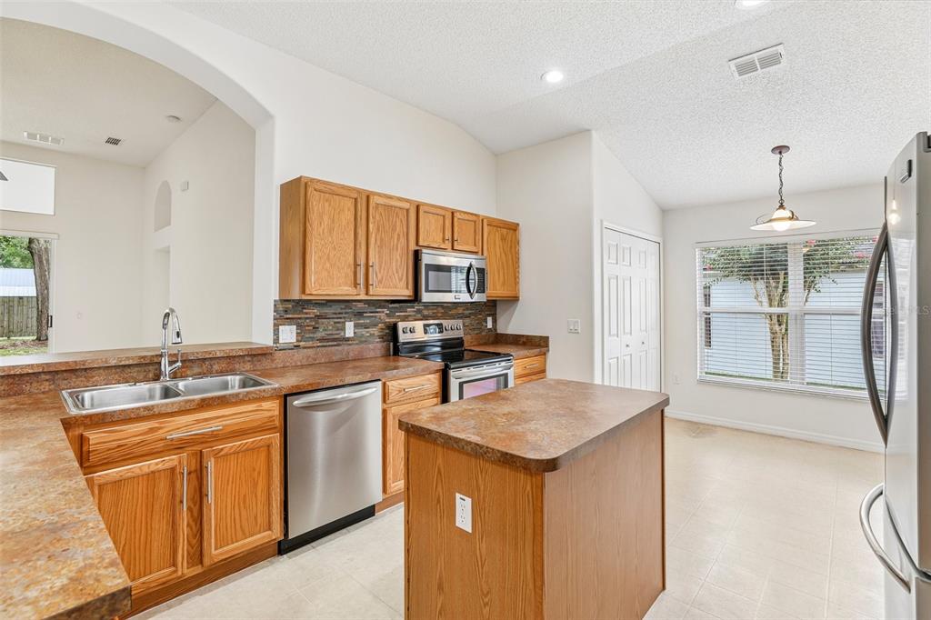 A kitchen with wood cabinets, laminate countertops, stainless steel appliances, and a central island — 30254 PGA DRIVE, SORRENTO, FL