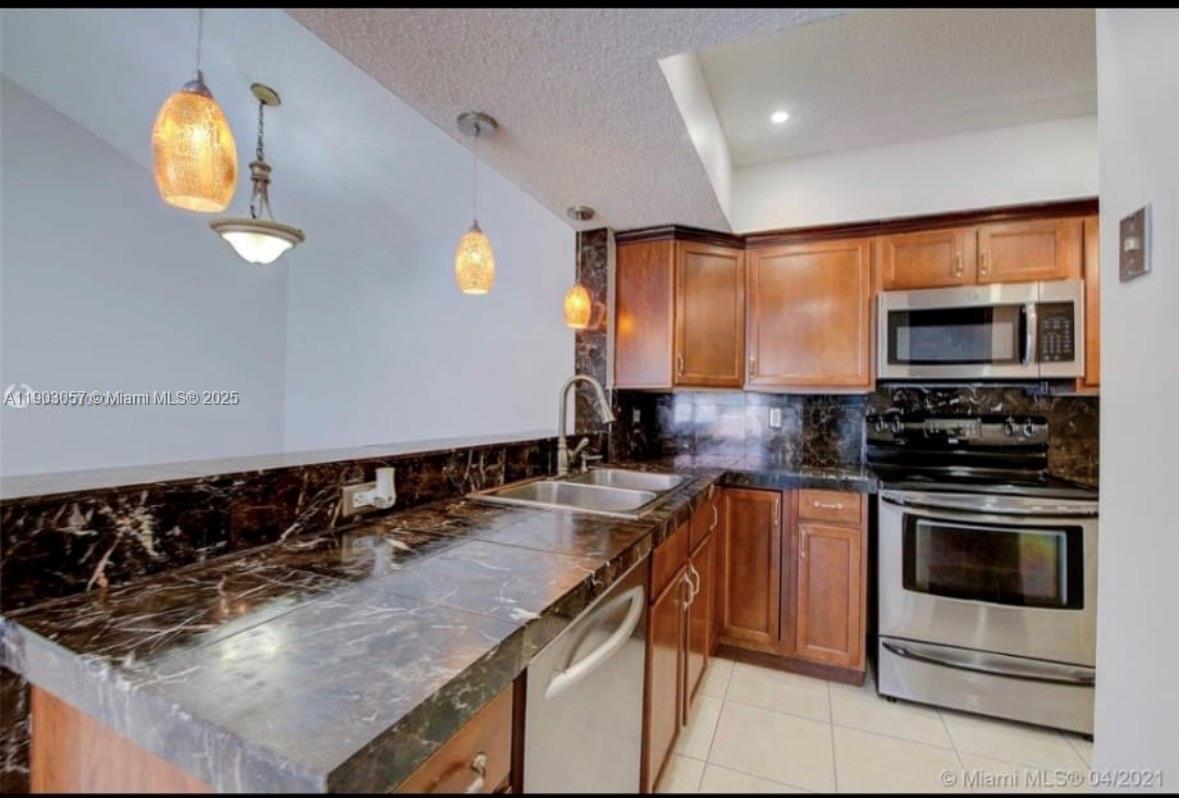 A kitchen with dark marble countertops, wooden cabinets, and stainless steel appliances — 18850 NW 57th Ave # 306, Hialeah FL 33015, HIALEAH, FL