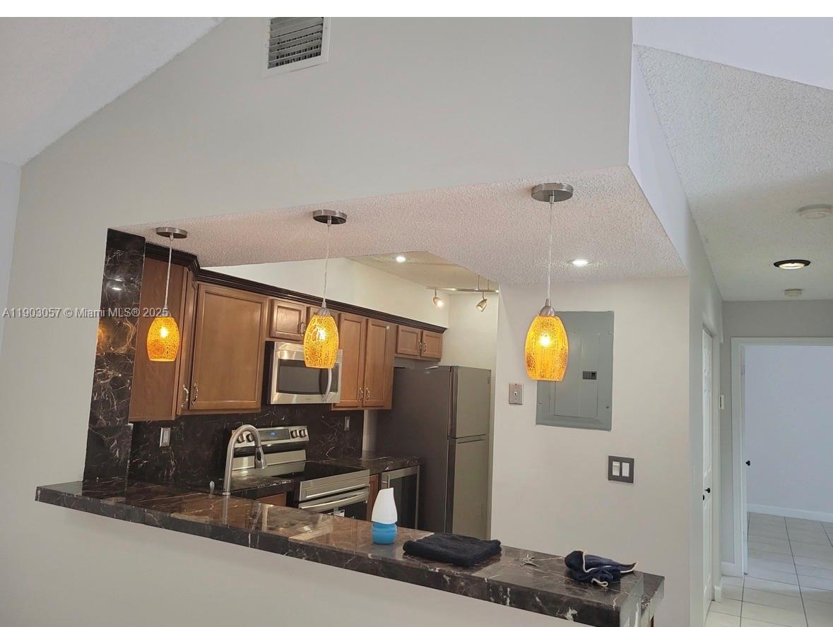 A kitchen features wood cabinets, dark marble countertops, and three pendant lights over a bar — 18850 NW 57th Ave # 306, Hialeah FL 33015, HIALEAH, FL