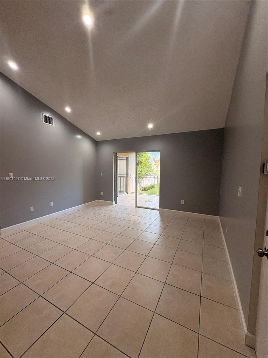 An empty living room features gray walls, tile flooring, recessed lighting, and a sliding glass door — 18850 NW 57th Ave # 306, Hialeah FL 33015, HIALEAH, FL