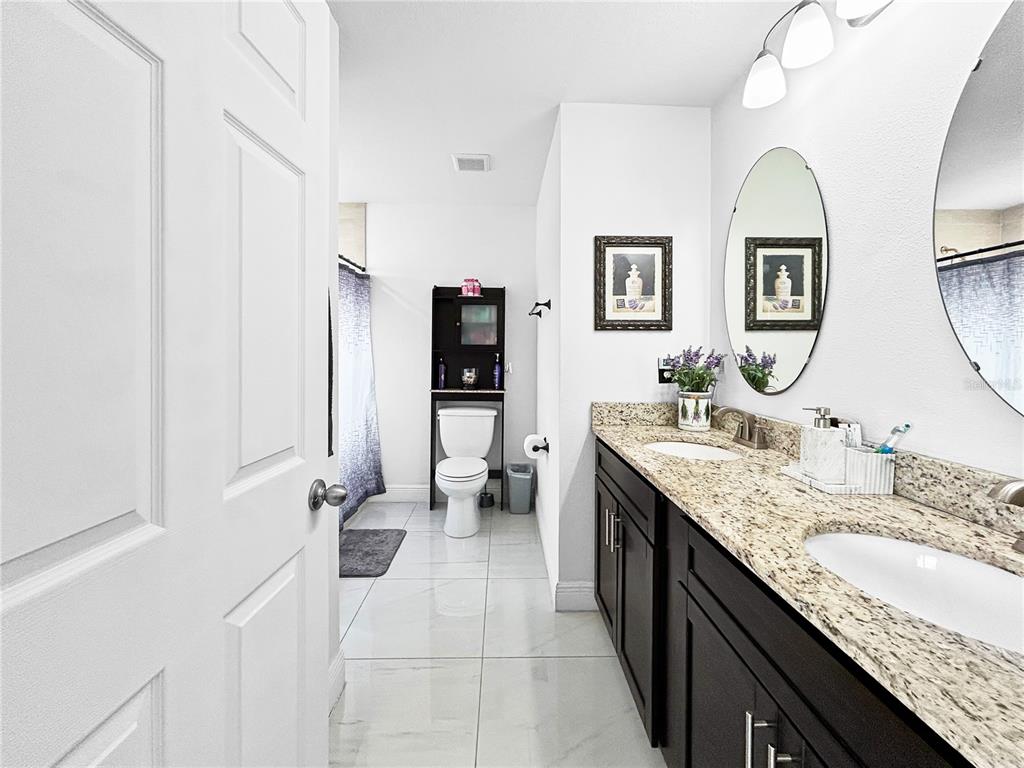 A bathroom features a double vanity with granite countertops, dark cabinets, and a toilet area — 1017 FRASER PLACE, POINCIANA, FL