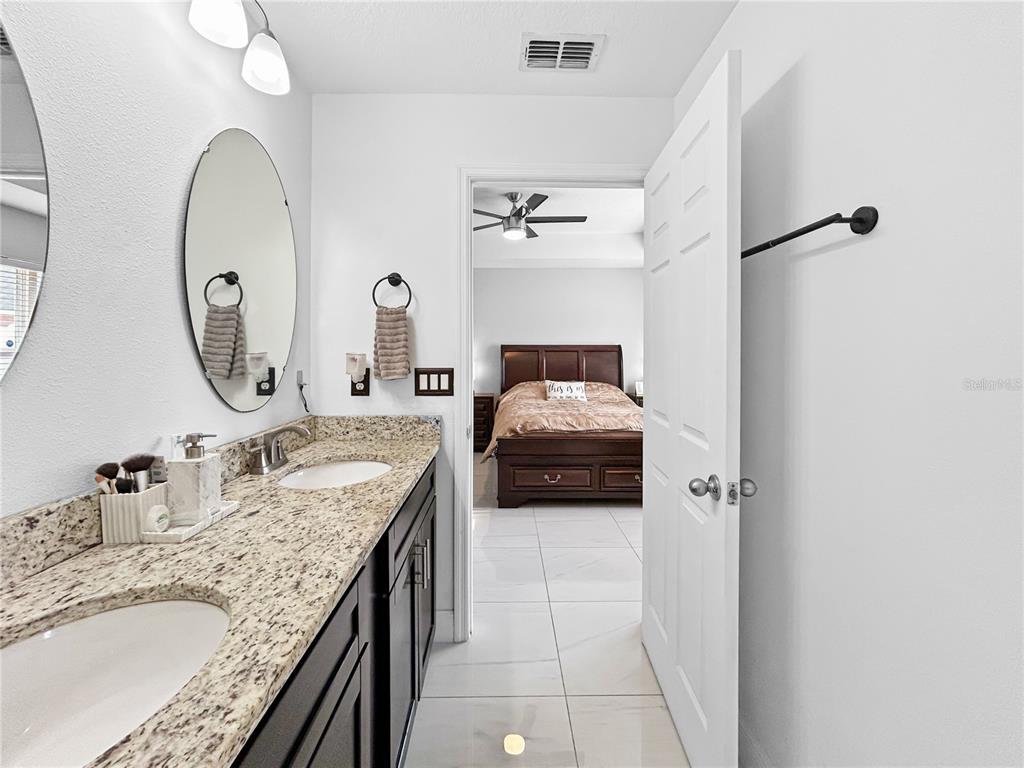 A bathroom with a double vanity and granite countertop leads into a bedroom with tile flooring — 1017 FRASER PLACE, POINCIANA, FL