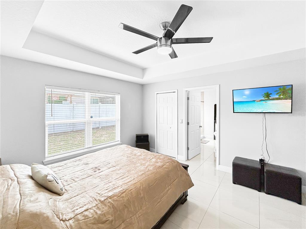 A bedroom features a bed, a ceiling fan, tiled floors, and a wall-mounted television — 1017 FRASER PLACE, POINCIANA, FL