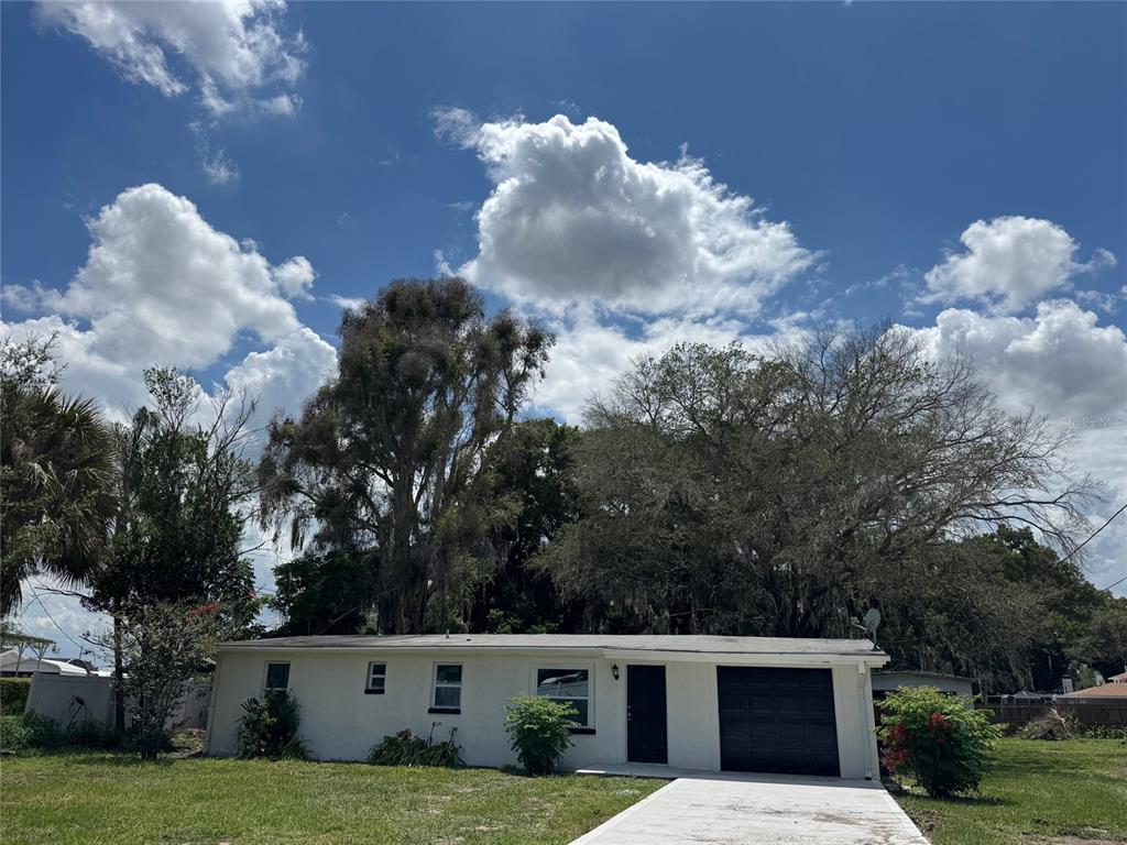 A single-story house with a white exterior, a black garage door, and large surrounding trees — 2121 GREENWAY DRIVE, WINTER HAVEN, FL