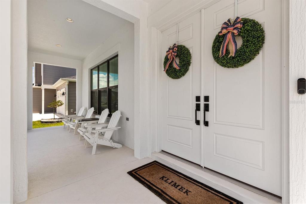 A covered front porch features white Adirondack chairs, double doors with wreaths, and a doormat — 7969 BYERS ST, MIDDLETON, FL