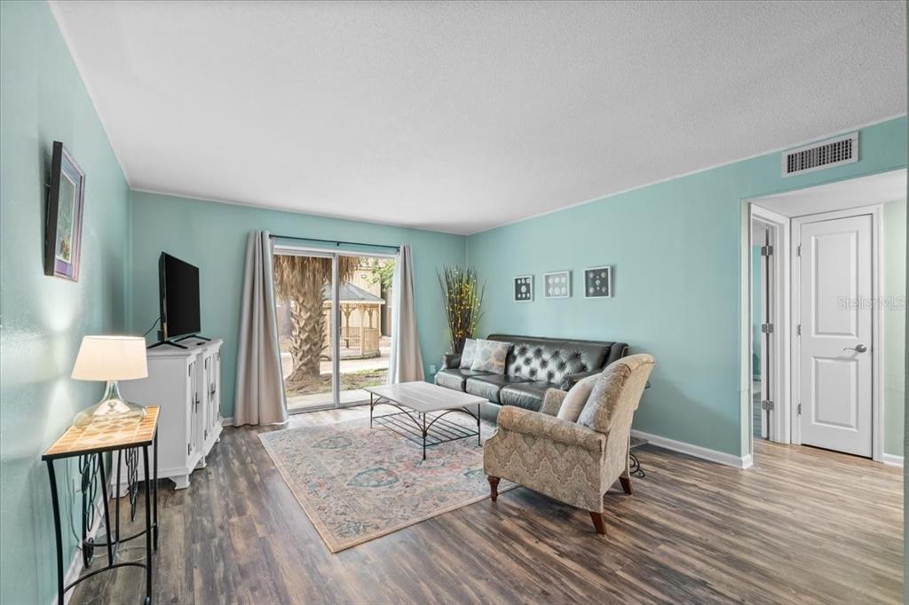 A living room features light blue walls, wood-look flooring, a sliding glass door, and furniture — 507 NW 39TH ROAD UNIT 110, GAINESVILLE, FL