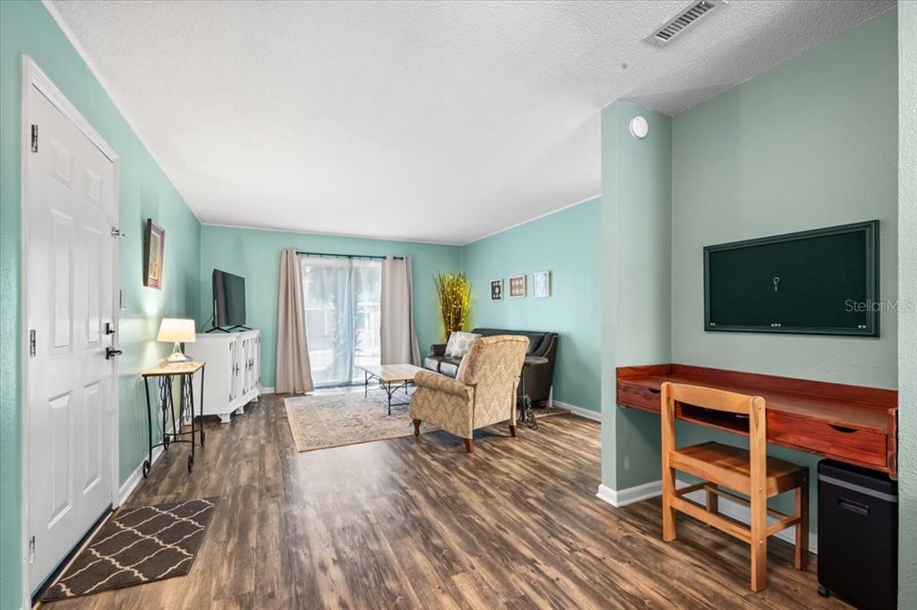 A living room features light blue walls, wood-look flooring, a desk area, and sliding glass doors — 507 NW 39TH ROAD UNIT 110, GAINESVILLE, FL