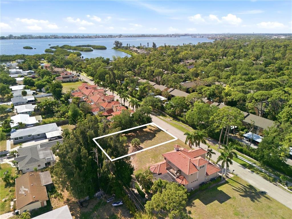 An aerial view shows a vacant rectangular lot situated between residential homes near a bay — 1740 ASSISI DRIVE, SARASOTA, FL