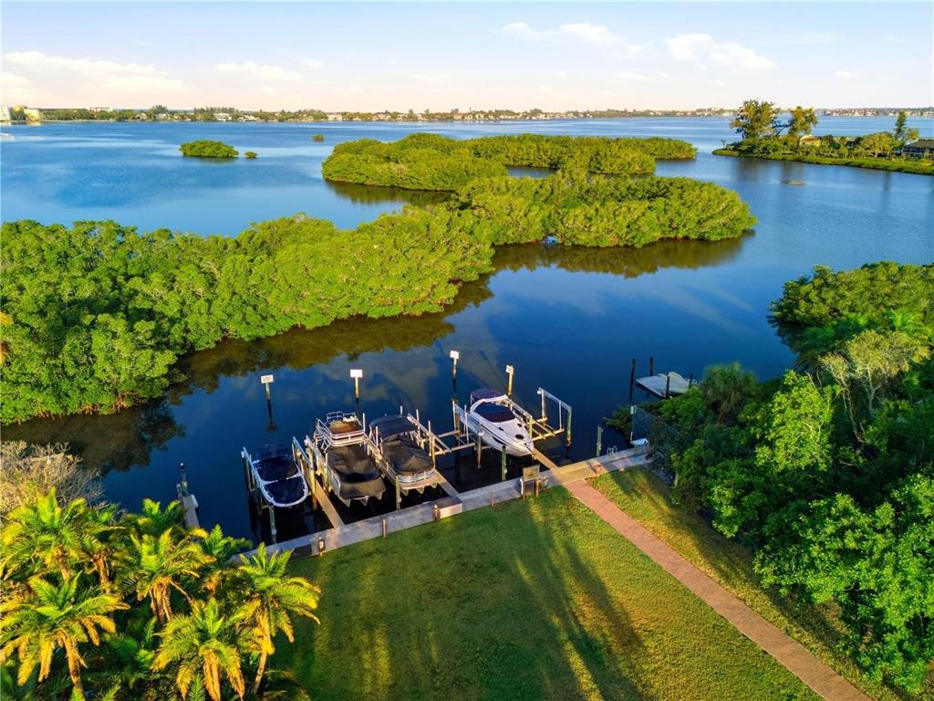 An aerial view shows a boat dock with three boats on a calm, mangrove-lined waterway — 1740 ASSISI DRIVE, SARASOTA, FL