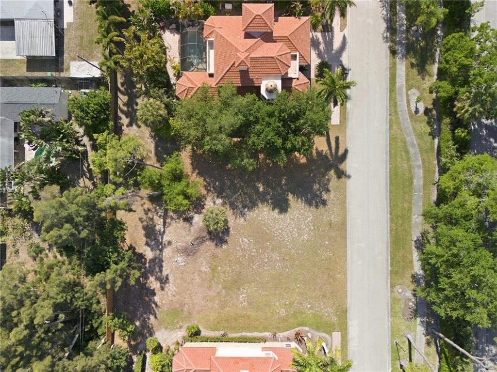 An aerial view shows a vacant residential lot situated between two houses with tiled roofs — 1740 ASSISI DRIVE, SARASOTA, FL