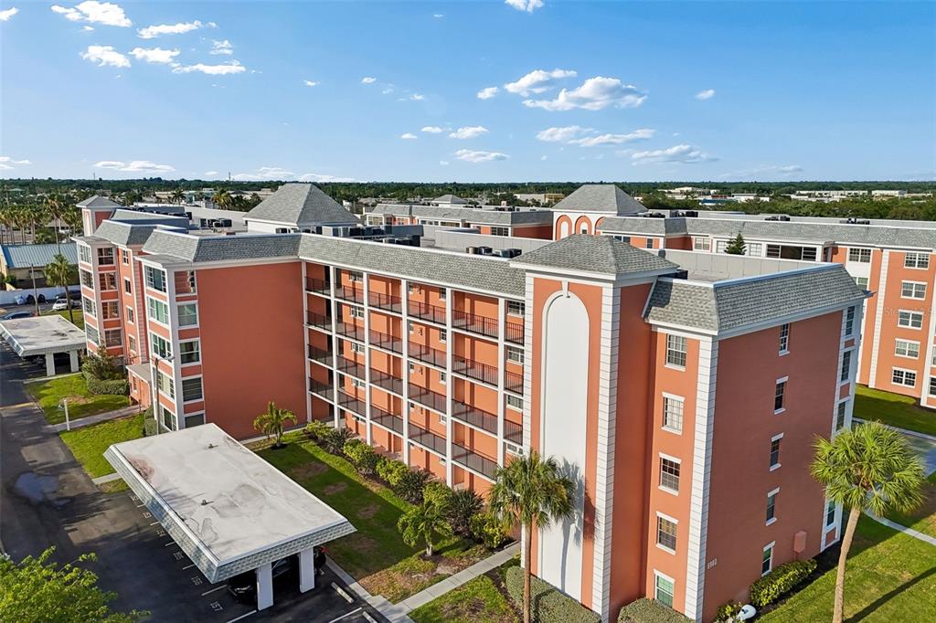 An aerial view of a multi-story orange apartment building with a covered parking entrance — 6960 20TH AVENUE N UNIT 501, ST PETERSBURG, FL