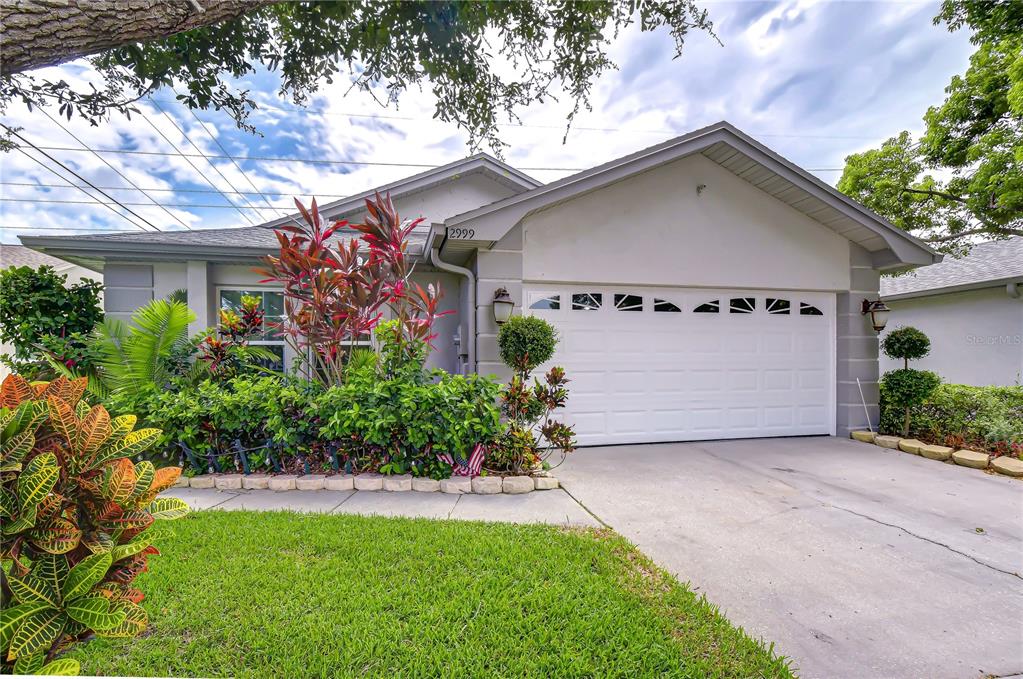 A single-story house with a white garage door, gray siding, and a landscaped front yard — 2999 BROOKFIELD LANE, CLEARWATER, FL