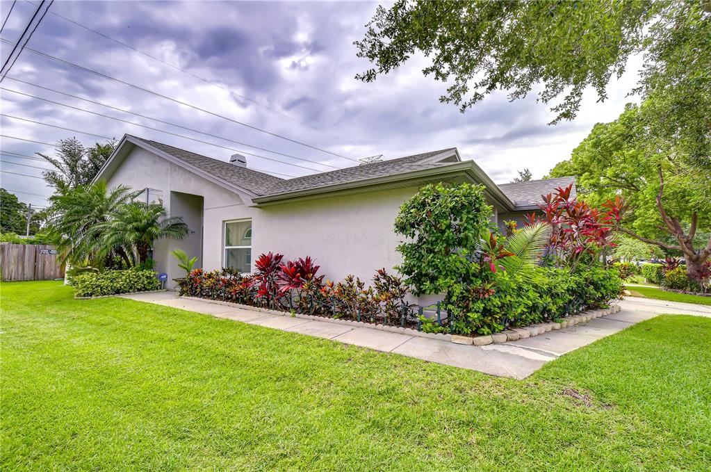 A single-story house exterior with a light-colored facade, a walkway, and landscaped garden beds — 2999 BROOKFIELD LANE, CLEARWATER, FL