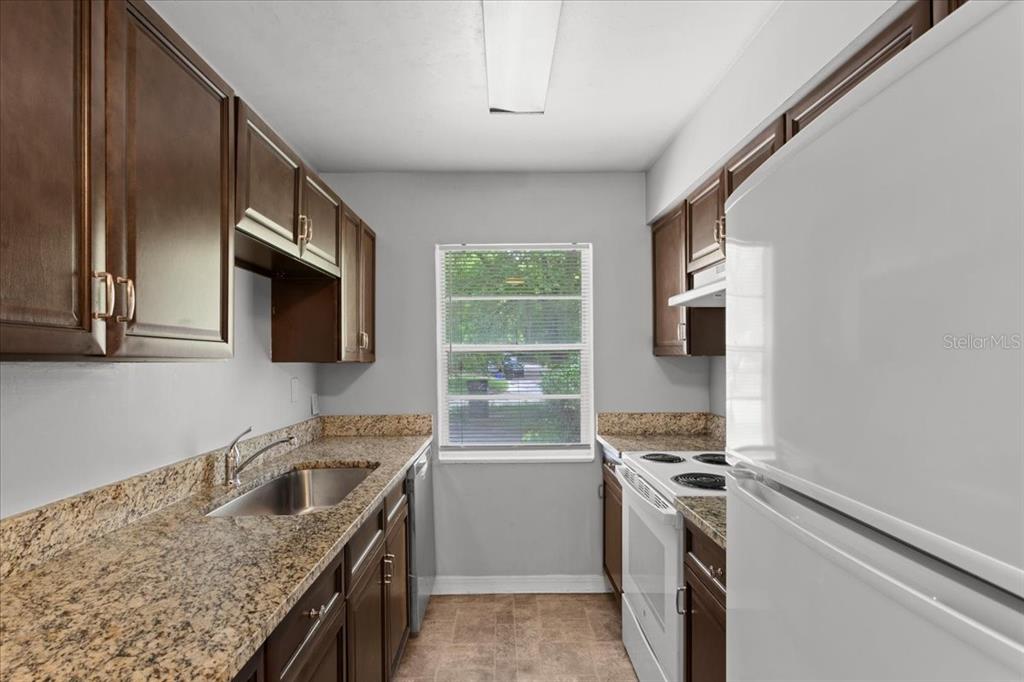 A galley kitchen features dark wood cabinets, granite countertops, and a white refrigerator — 1816 SW 70TH TERRACE, GAINESVILLE, FL