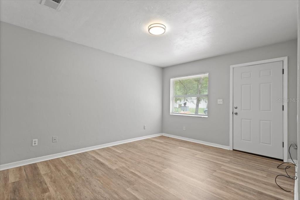 A room with light gray walls, wood-look flooring, a window, and a white entry door — 1816 SW 70TH TERRACE, GAINESVILLE, FL
