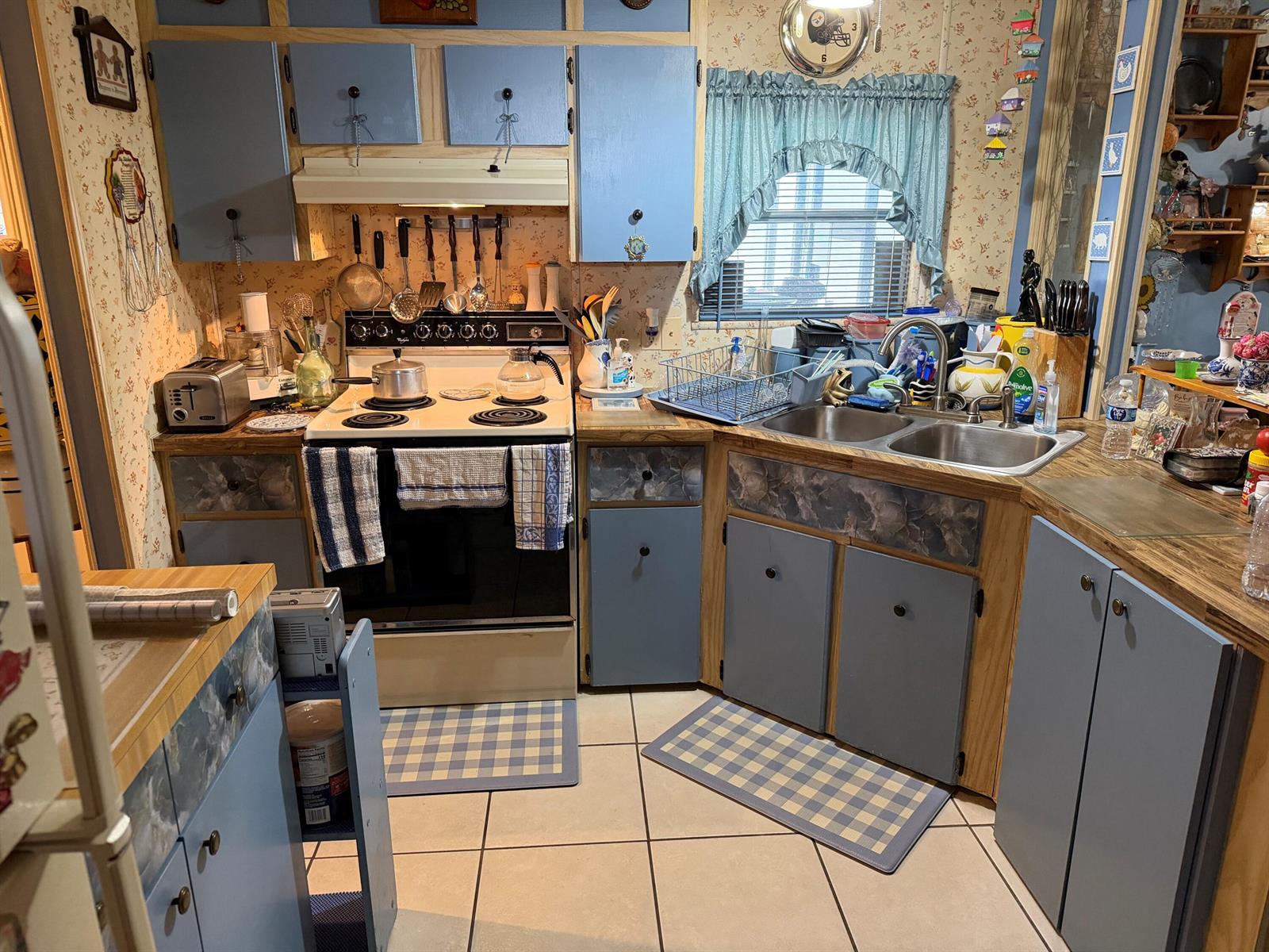 A kitchen features blue cabinets, floral wallpaper, a white stove, and a double-basin sink — 5230 SW 29th Terrace, Dania Beach FL 33312, DANIA BEACH, FL