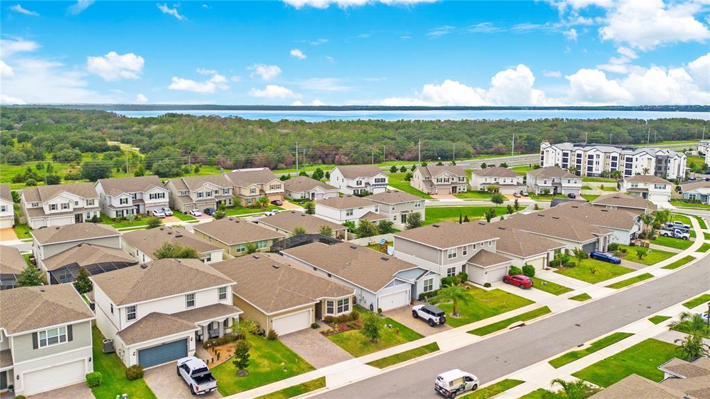 An aerial view shows a suburban neighborhood with houses, streets, and a lake in the distance — 7635 TAORMINA WAY, CLERMONT, FL