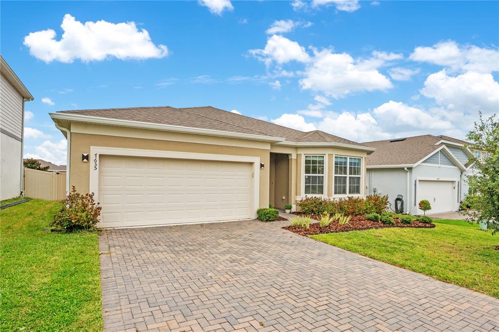 A single-story house with a beige stucco exterior, a two-car garage, and a paver driveway — 7635 TAORMINA WAY, CLERMONT, FL