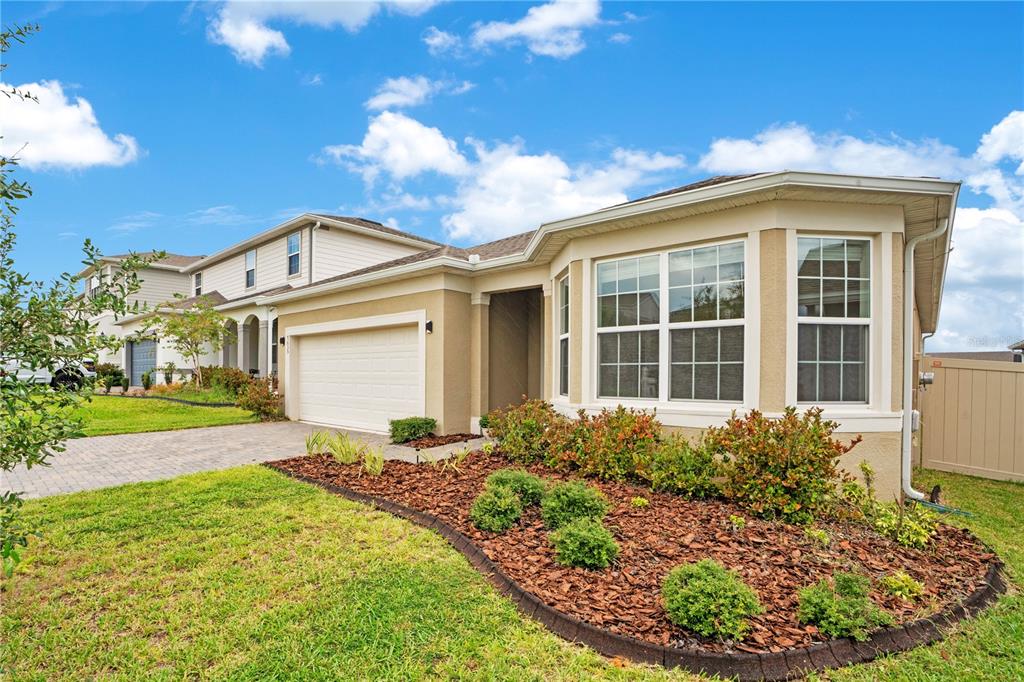 A tan single-story house with a two-car garage, bay window, and landscaped front yard — 7635 TAORMINA WAY, CLERMONT, FL