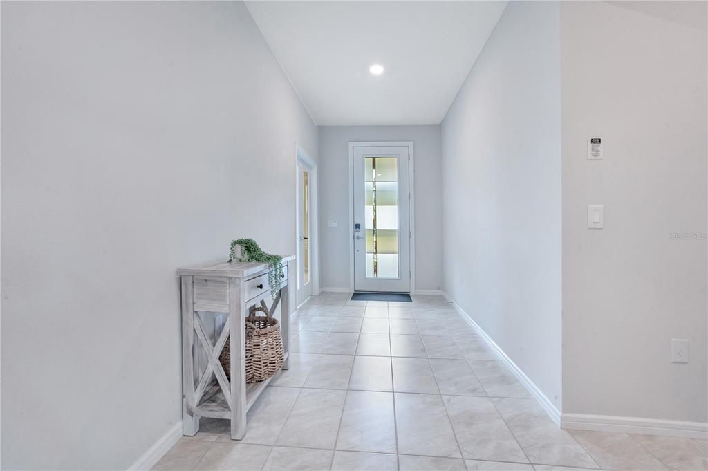 A bright entryway features light-colored tile flooring, a white console table, and a modern glass-paneled door — 7635 TAORMINA WAY, CLERMONT, FL