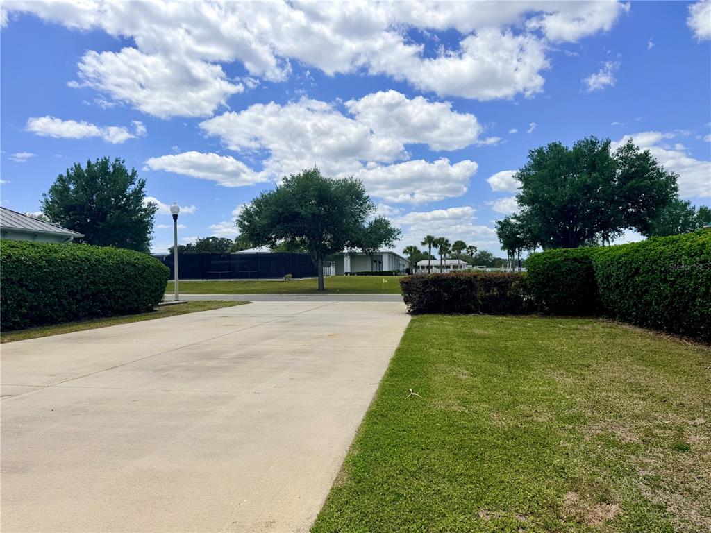 A concrete driveway leads toward a grassy area with hedges and trees under a cloudy sky — 9589 SE 49TH TERRACE, WEBSTER, FL