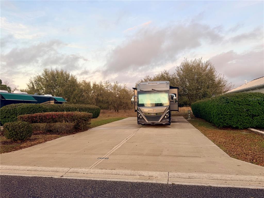 A large recreational vehicle is parked on a concrete driveway between two manicured hedges — 9589 SE 49TH TERRACE, WEBSTER, FL