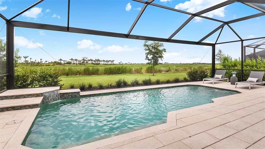 A screened-in pool patio features a waterfall, lounge chairs, and a view of a field — 8220 SUMMER NIGHT ROAD, SARASOTA, FL