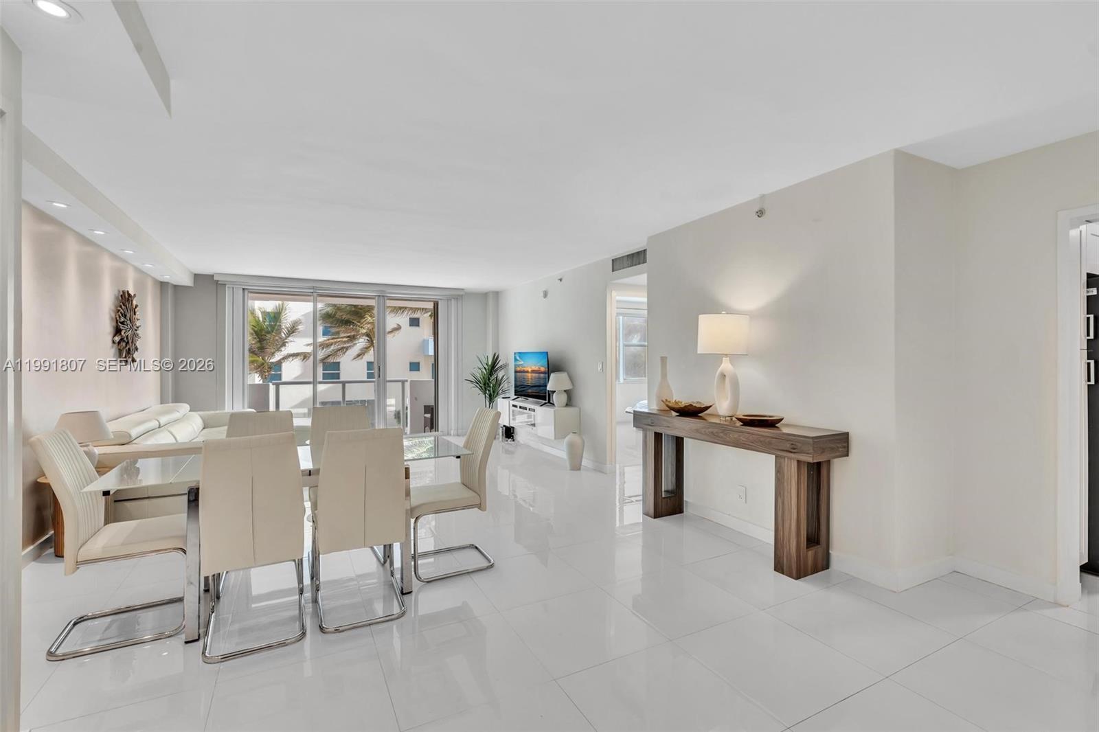 A bright dining and living area features white tile floors, modern furniture, and a balcony — 9195 Collins Ave # 303, Surfside FL 33154, SURFSIDE, FL