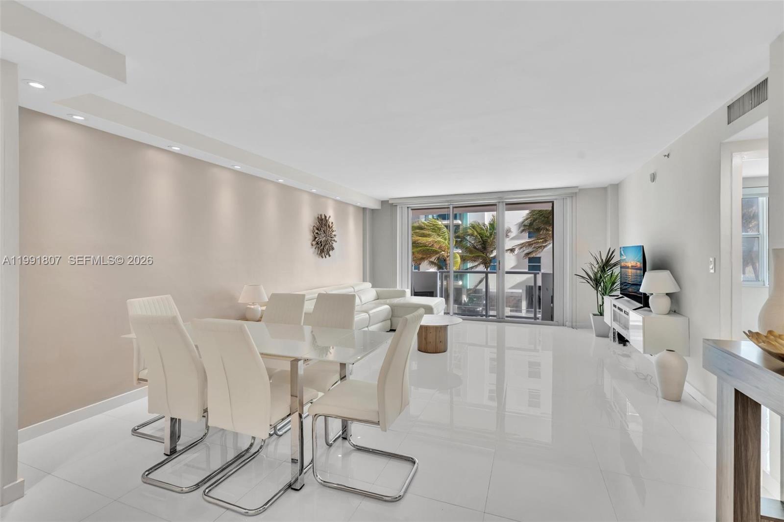 A dining and living area features white tile floors, modern furniture, and a balcony view — 9195 Collins Ave # 303, Surfside FL 33154, SURFSIDE, FL