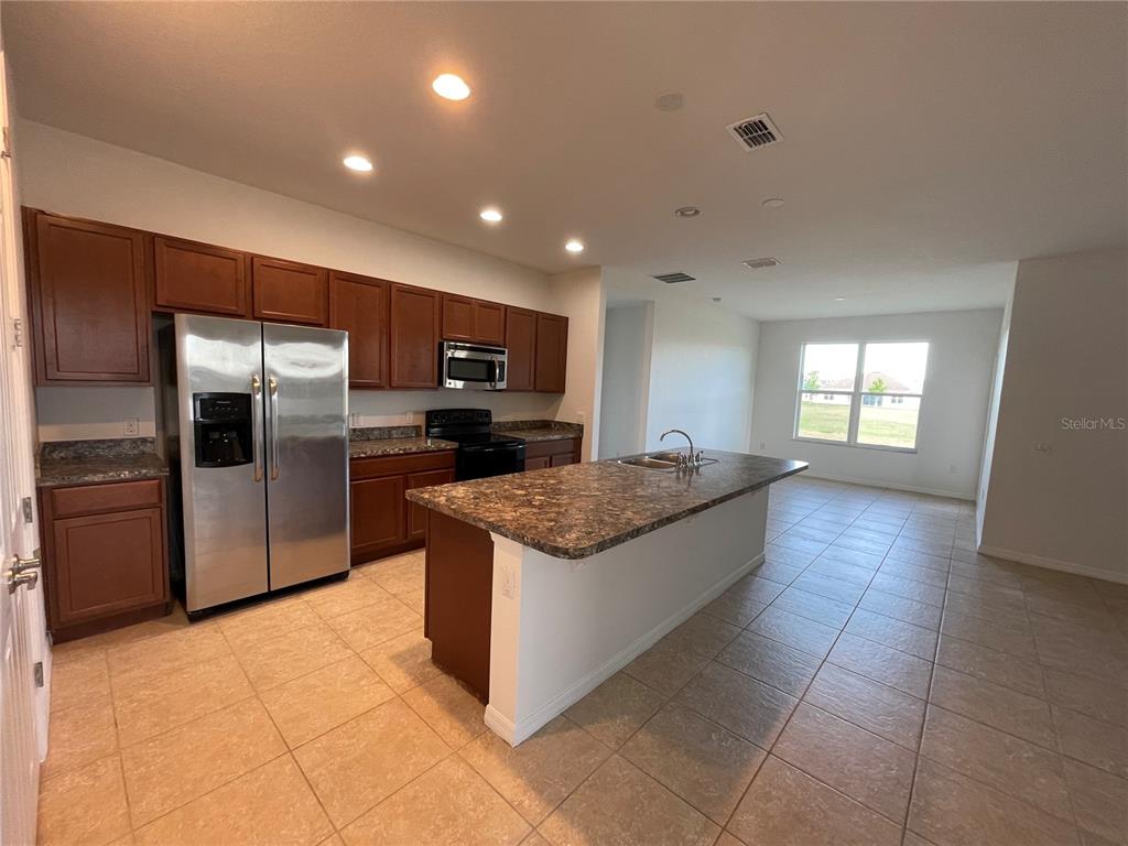 A kitchen features dark wood cabinets, granite countertops, a center island, and stainless steel appliances — 2269 WAUKEGAN DRIVE, KISSIMMEE, FL