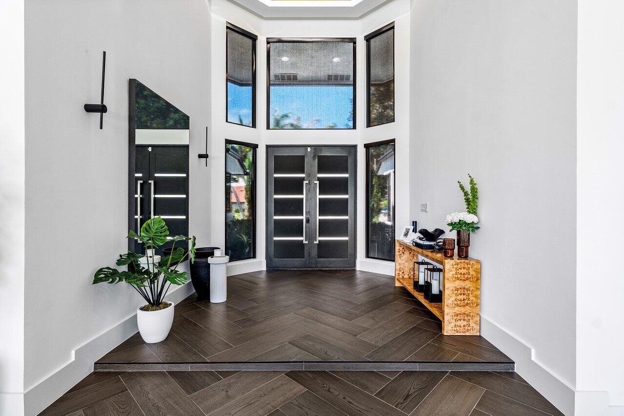 A modern entryway features dark herringbone wood floors, a double front door, and large windows — 4825 Bocaire Boulevard, Boca Raton FL 33487, BOCA RATON, FL