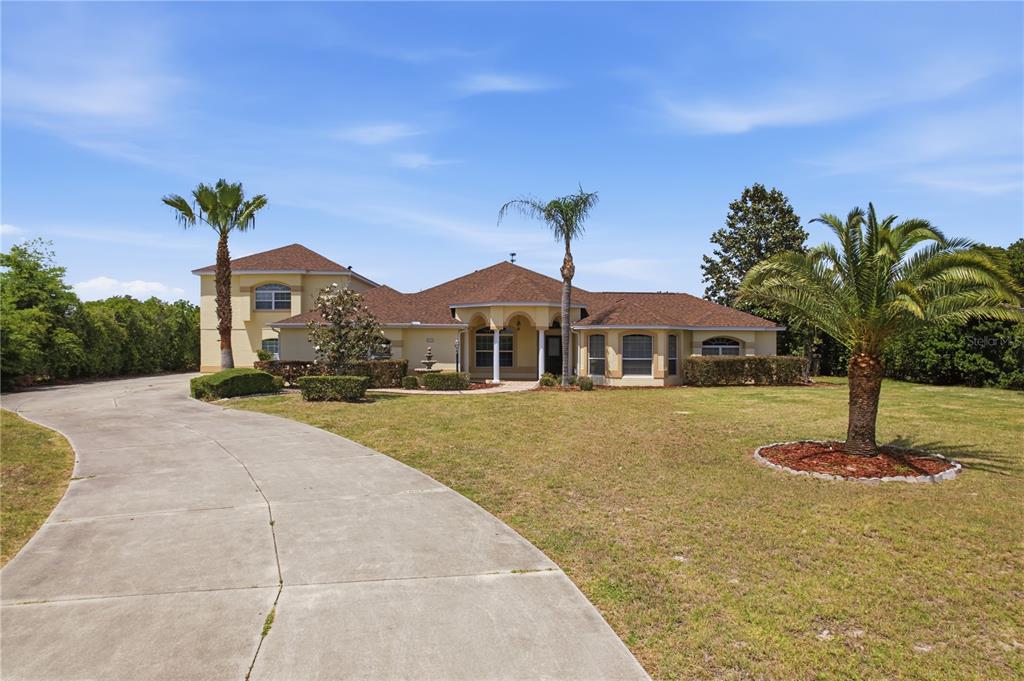 A tan, single-story house with a two-story section, a concrete driveway, and several palm trees — 4141 COUNTY ROAD 121D, WILDWOOD, FL